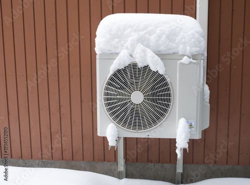 outdoor home air conditioner unit covered with fresh white snow in winter