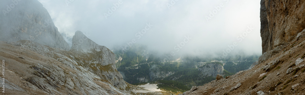 Obraz premium Panoramic foggy alpine valley framed by steep limestone cliffs in Dolomites mountains Italy