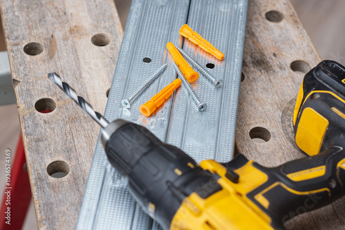 Φωτογραφία Cordless drill with drill bit, plastic wall plugs and metal screws on galvanized metal profile
