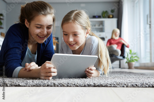 Teo sisters lying on floor, playing with digital tablet