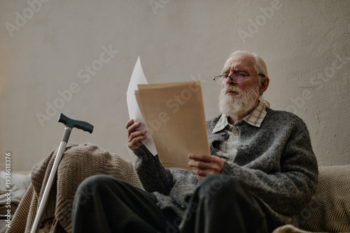 Εκτύπωση καμβά Senior Caucasian man sitting indoors reading documents while holding papers in h