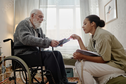 Obraz na plátne Middle aged Black woman social worker assisting senior Caucasian man with disabi