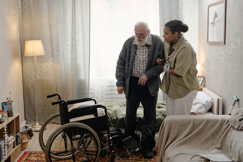 Quadro em tela Black woman social worker assisting senior Caucasian man with disability standin