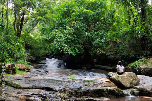 Woman relaxing by waterfall in lush thai forest