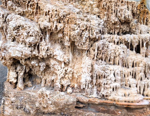 Mineral Cascades in Stone: close-up view of intricate mineral formations layered across a rugged rock surface. Cream and beige deposits create drip-like textures resembling frozen waterfalls