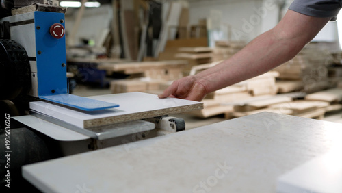 Bild auf Leinwand Worker processing a laminated particle board panel on industrial machinery in a furniture workshop