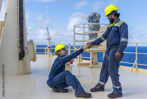 Schilderij op canvas One ship officer helping a colleague up from the deck of a commercial vessel, demonstrating teamwork and support at sea