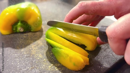 close up of yellow and green peppers being sliced with knife on cutting board