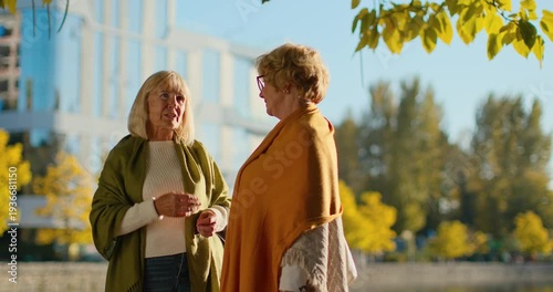 Two cheerful senior friends enjoying a conversation outdoors in a city park