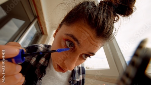 Female model crafting makeup look using smartphone camera under morning sun