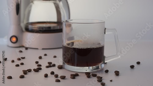 Glass mug with freshly brewed coffee, coffee maker in the background