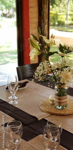 Mesa de restaurante elegante con arreglos florales de lirios blancos, copas de cristal y luz natural de jardín