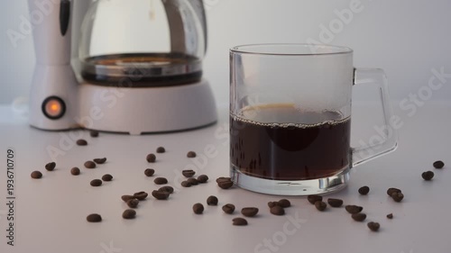 Glass mug with freshly brewed coffee, coffee maker in the background