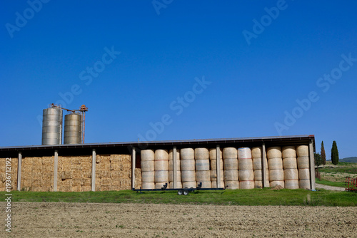 Hay Bales Stored in Agricultural Barn with Silos in Tuscan Countryside, Italy