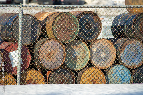 Rusty steel barrels stacked by a chain link fence during winter