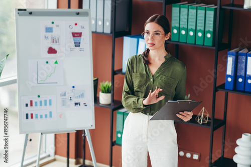 Fotografie Businesswoman giving a presentation in a modern office with charts and clipboard