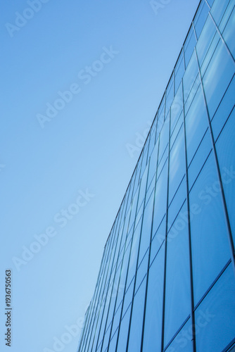 Fotografie Reflective business office building facade made of glass and clear blue sky