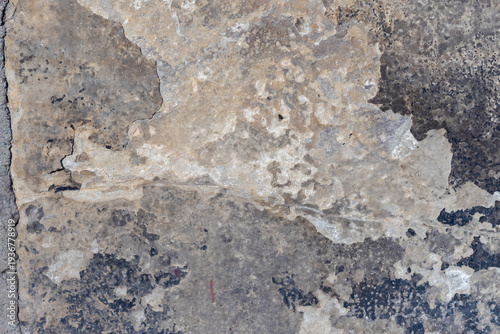 A close-up of a weathered plaster wall showing peeling paint, cracks and roug...