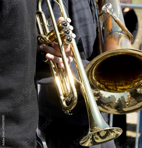 Musician holds a brass trumpet and a larger instrument. 