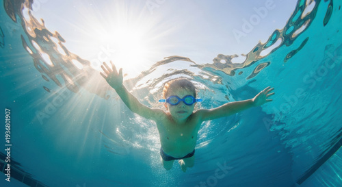 Young boy swimming underwater in a sunny pool with goggles