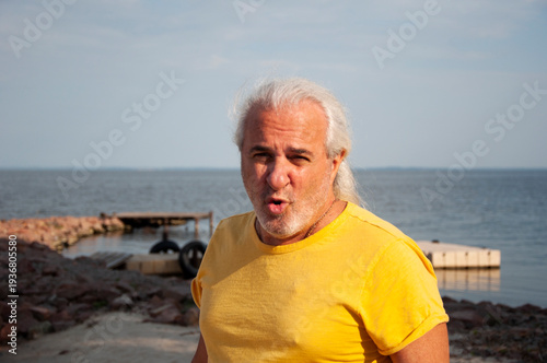 Mature man by ocean horizon during sunset. Authentic masculine style. Retired man enjoying peaceful seaside view. Senior traveler relaxing by coast. Senior lifestyle. Relaxed vacation lifestyle