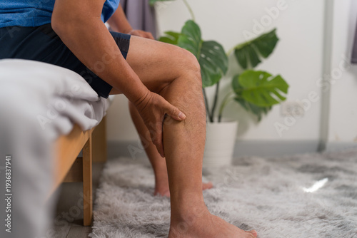 Bild auf Leinwand Senior Asian man suffering from varicose veins leg pain sitting on bed at home
