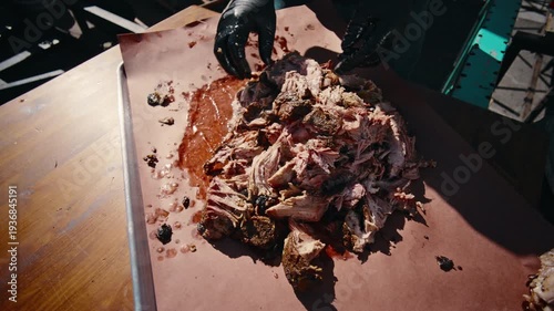 Top-down slow-motion shot of shredded smoked pulled pork piled on pink butcher paper in a metal tray at an outdoor BBQ setting