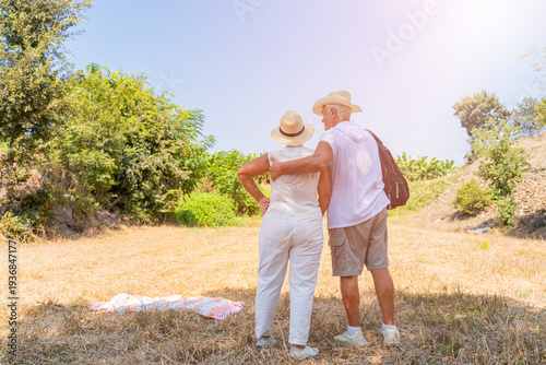 Senior couple sitting together on dry grass field in straw hats enjoying summer nature outdoors
