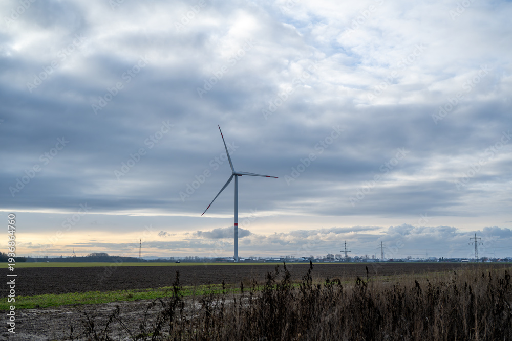 Obraz premium A wind turbine is in the middle of a field with a cloudy sky