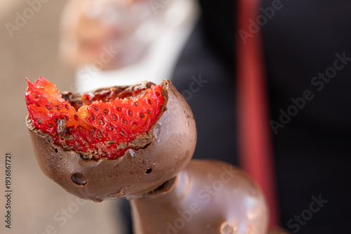 Bitten chocolate-covered strawberry held. Juicy red interior contrasts with rich chocolate. 