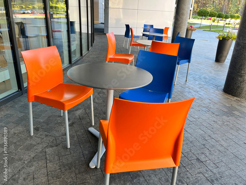 Orange and Blue Chairs and Round Tables in Empty Outdoors Street Cafe.