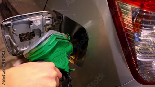 close up hand holding green nozzle pumping unleaded gasoline petrol into car tank night gas station energy crisis global inflation rising oil prices economy fossil fuel transport cost concept