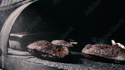 Top-down cinematic view inside a dark barrel smoker showing four large briskets resting on the grill grate in moody dramatic lighting