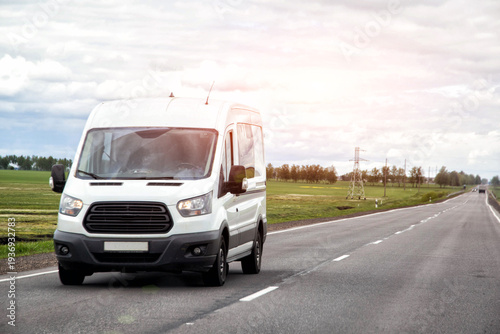 White commercial cargo van traveling on rural asphalt road during daytime under overcast sky, transportation of goods and people between cities, delivery vehicle moving