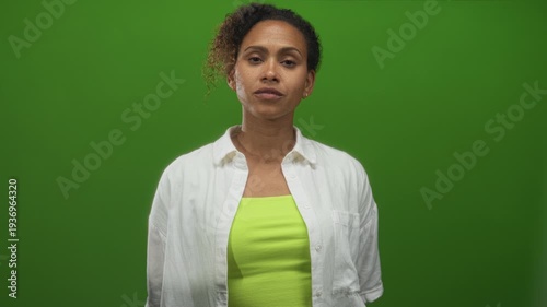 Woman in green studio looking to the side with exposed neck and collarbone, wearing white shirt and neon tank top; contemplation.
