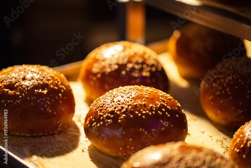 Warm golden brown brioche style buns with sesame seeds fresh from oven display. Delicious baked goods ready for consumption or preparation.