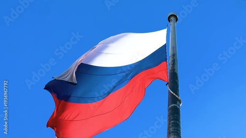 Russian national flag fluttering on a flagpole against a clear blue sky on a sunny day