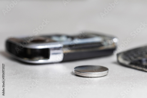 Foto Automotive key fob and new button battery for power replacement, illustrating vehicle electronic component maintenance and repair procedure, close-up shot on light background