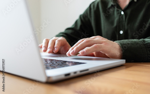 Mans hands with laptop closeup in home office at working desk. Remote job, business and searching information concept.