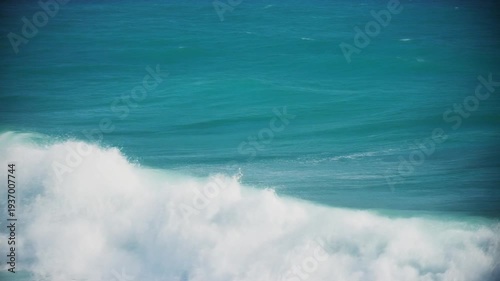 Aerial view of a cresting wave over tranquil blue-green sea, capturing the gentle foam and calm water in a peaceful perspective