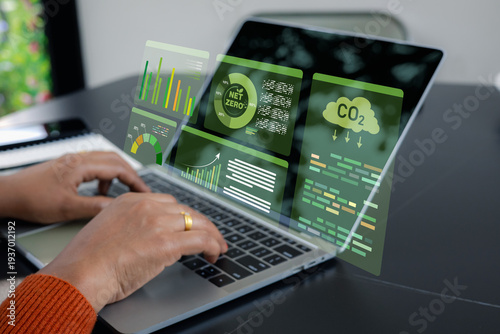 Businesswoman using laptop with virtual Net Zero and CO2 emission reduction dashboard. Concept of ESG sustainability, green energy management and carbon neutral business technology.