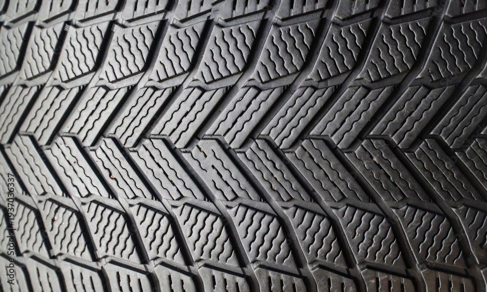 Fototapeta premium Winter friction tires with tread pattern or close-up texture. The concept of driving safety in winter on a slippery road. Winter studless car tires on a black background in close-up. 
