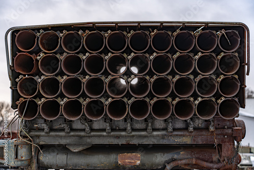 View of multiple launch rocket system with dark, circular tubes and weathered metal, standing stark against a muted sky, Kyiv, Kyiv, Ukraine.