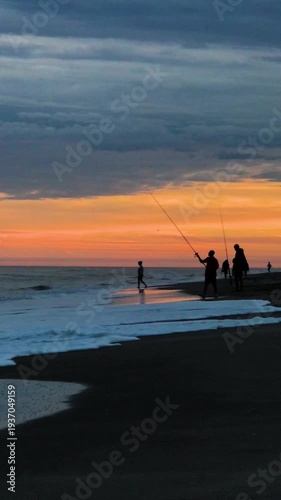 Silhouette of Men Fishing from Sandy Beach at Evening Sunset a Summer Day