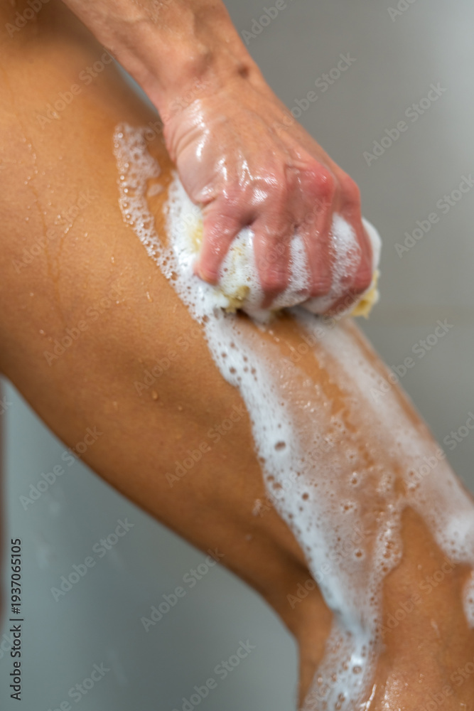 Fototapeta premium Woman washing leg with natural sponge in shower, body hygiene routine, skincare and wellness concept, daily cleansing, healthy lifestyle, self care, freshness