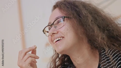 Hotel room closeup smiling guest enjoying snack, playful expression, glasses glinting in warm light, spontaneous laugh, vacationer relishing quiet comfort, candid hospitality moment