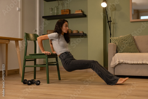 Foto Fit woman performing triceps dip exercise using chair at home, bodyweight streng