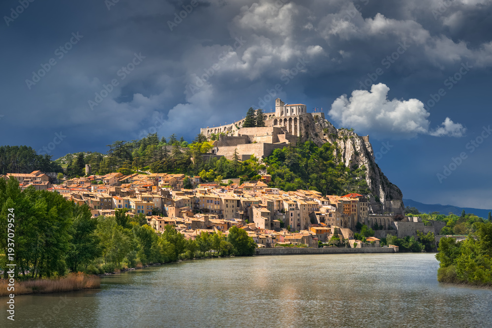 Fototapeta premium Sisteron Citadel above the Durance River, Alpes-de-Haute-Provence, France. Cliffside fortification and historic town under storm clouds