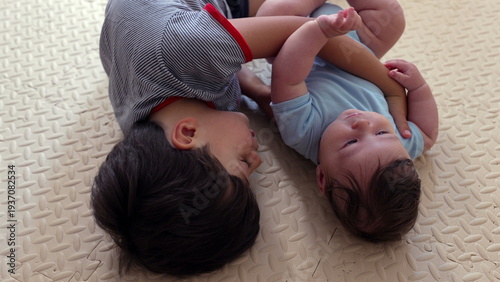 Photography Young boy lying on mat embracing baby sibling, tender brotherly bond, affectiona