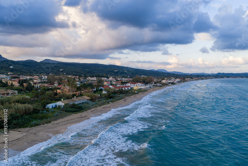 Aerial view of Acharavi coastal town in Corfu, Greece, with rough sea waves and dramatic cloudy sky.